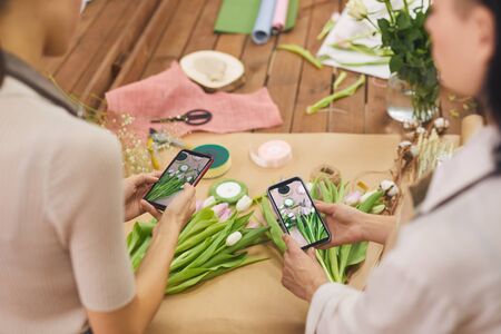 High angle view at two women taking smartphone photo of tulip flowers while working in flower shop, copy spaceの写真素材