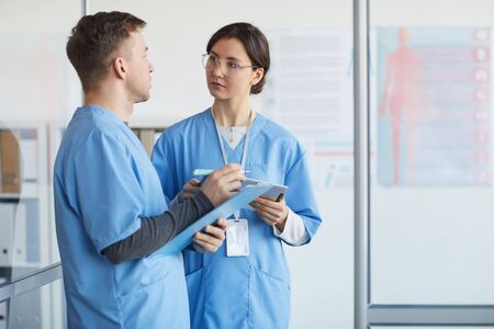 Waist up portrait of two medics holding clipboards while standing in medical office interior, copy spaceの写真素材