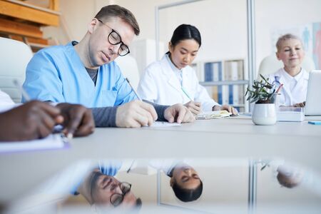 Low angle view at group of doctors sitting round table during medical council or conference in clinic, copy spaceの写真素材