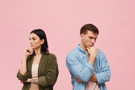 Waist up portrait of frustrated couple standing back to back against pink background, copy spaceの写真素材