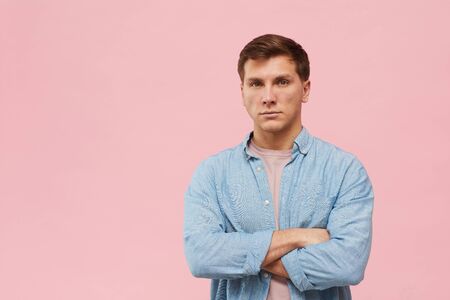 Waist up portrait of adult man standing with arms crossed and looking at camera while posing against...