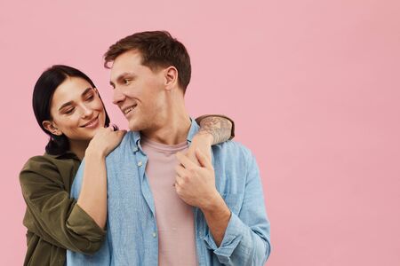 Waist up portrait of happy young couple posing against pink background in studio, copy spaceの写真素材