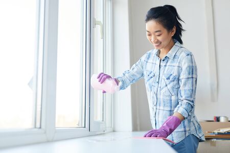 Waist up portrait of Smiling woman washing windows during Spring cleaning, focus on female hands wearing pink gloves, copy spaceの写真素材