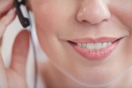 Extreme close up of unrecognizable call center operator wearing headset, focus on pleasant female smile, copy spaceの写真素材