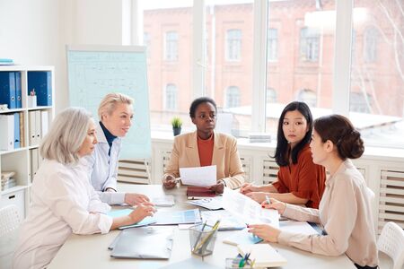 Multi-ethnic group of successful businesswomen discussing project while sitting at table against...