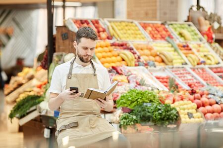 Portrait of bearded man calling supplier while selling fresh fruits and vegetables at farmers market, copy spaceの写真素材