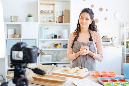 Attractive food vlogger preparing dough for baking it while shooting video on camera