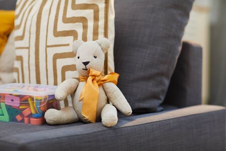 Cute teddy bear stuffed toy with yellow satin ribbon around its neck sitting on sofa, no people shot