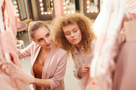 High angle portrait of two young women choosing dresses on rack in clothing boutique, copy spaceの写真素材