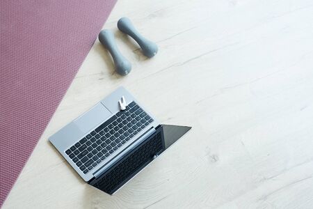 Minimal background image of yoga mat and dumbbells by computer laptop on wooden floor, online workout at home concept, copy spaceの写真素材
