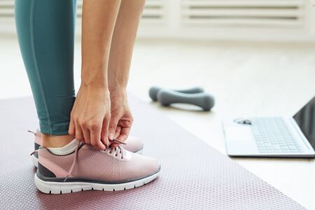 Side view close up of fit young woman tying shoe laces while standing on yoga mat ready for online workout at home, copy spaceの写真素材