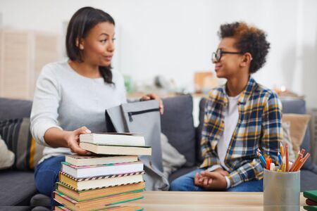 Portrait of young African-American woman talking to son while holding books for homeschooling, focus on foreground, copy spaceの写真素材