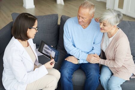 High angle portrait of female doctor consulting senior couple on lung condition while discussing x-ray image in clinicの写真素材