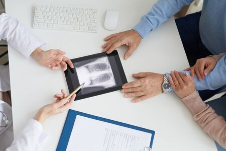 Close up of unrecognizable senior couple listening to female doctor and looking at lung x-ray image...