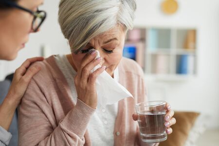 Close up portrait of elegant senior woman crying during therapy session and holding glass of water with female psychologist comforting herの写真素材