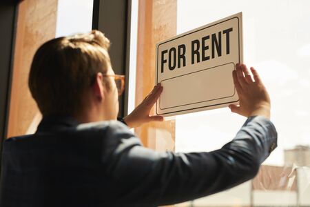Back view at real estate agent hanging FOR RENT sign on window of house or apartment, copy spaceの写真素材