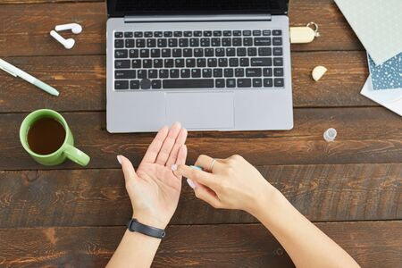 Top down view at unrecognizable young woman using hands sanitizer while using laptop at home office,...