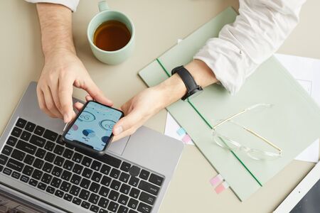 Top view closeup of unrecognizable man using smartphone while working at home office in minimal...