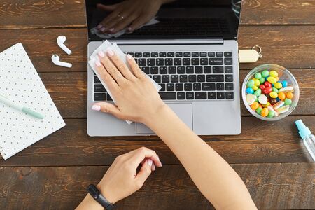Top down view at unrecognizable young woman sanitizing laptop with cleaning wipe while working at...