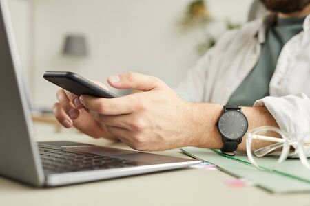 Side view closeup of unrecognizable man using smartphone while working at home office in minimal...