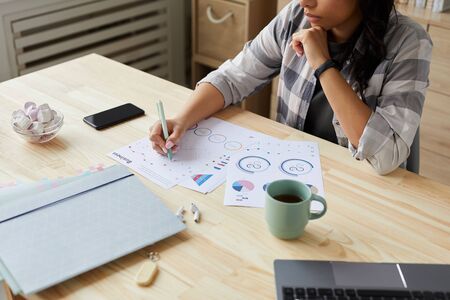 Cropped portrait of young mixed-race woman drawing graphs and charts while planning project at home...