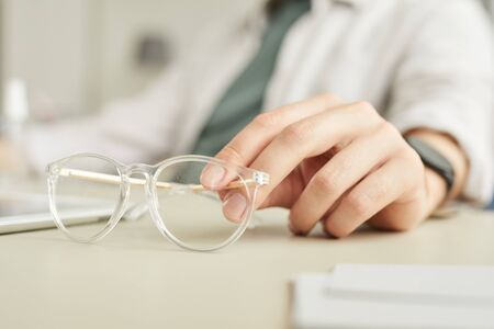 Minimal close up of hand holding crystal clear glasses while working at desk in office, copy space