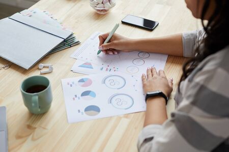 High angle close up of young mixed-race woman drawing graphs and charts while planning project at...