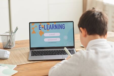 Back view at little boy studying at home with focus on laptop screen with e-learning website , copy...