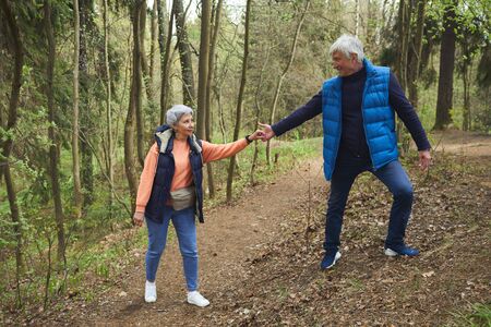 Full length portrait of active senior couple helping each other while climbing on hill during hike...