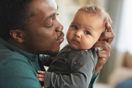 Close up portrait of cute mixed-race baby looking at camera while sitting in fathers arms at home, copy spaceの写真素材