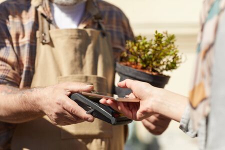 Close up of unrecognizable female customer holding bank card while paying via NFC in plantation outdoors, copy spaceの写真素材