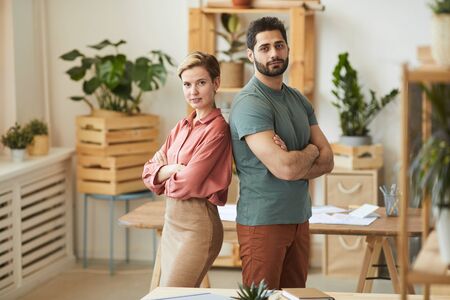 Waist up portrait of two sucessful entrepreneurs standing back to back while posing confidently in office, copy spaceの写真素材
