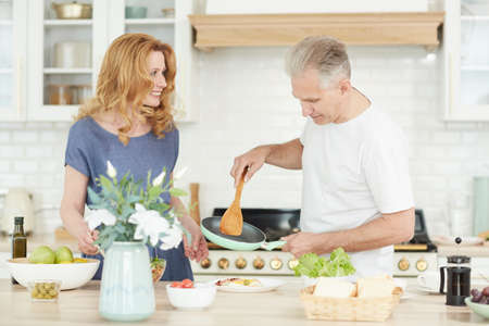 Waist up portrait of cheerful mature couple enjoying cooking together at home in white kitchen interior, copy spaceの写真素材