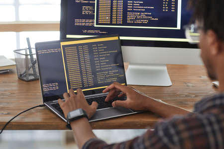Back view at African-American IT developer typing on keyboard with black and orange programming code...