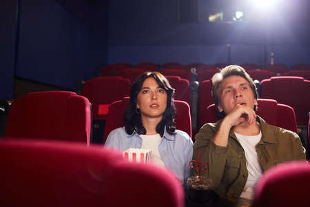 Portrait of young couple watching movie in cinema while enjoying private viewing in empty hall, copy spaceの写真素材