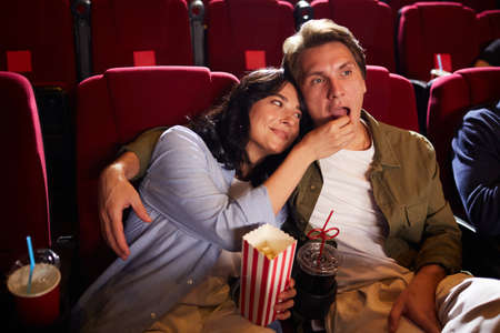 High angle portrait of carefree young couple watching movie in cinema theater and eating popcorn, copy spaceの写真素材