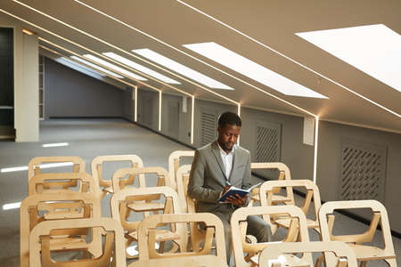 Portrait of successful African-American businessman writing in note pad while sitting in audience of...