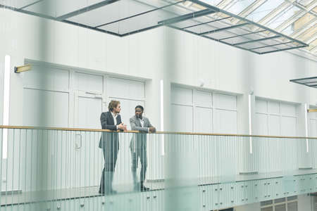 Wide angle view at two successful businessmen wearing suits standing on glass balcony in contemporary office building, copy spaceの写真素材