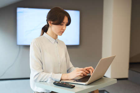 Waist up portrait of young businesswoman typing on laptop keyboard while working at standing table...