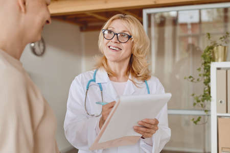 Warm-toned waist up portrait of cheerful female doctor talking to bald patient during consultation on alopecia and cancer recovery, copy spaceの写真素材