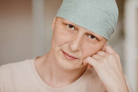 Warm-toned head and shoulders portrait of mature bald woman wearing headscarf and looking at camera...
