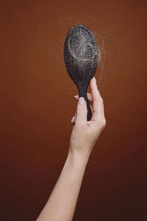 Vertical background image of female hand holding brush full of hair against brown background in studio, alopecia and hair loss concept, copy spaceの写真素材