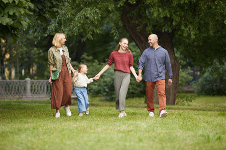 Full length portrait of modern carefree family with two kids holding hands while walking towards...