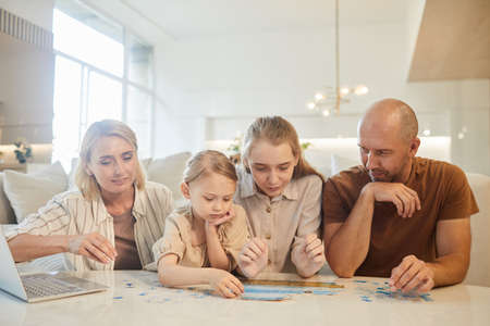 Warm-toned portrait of modern family with two kids solving puzzle together while enjoying time...