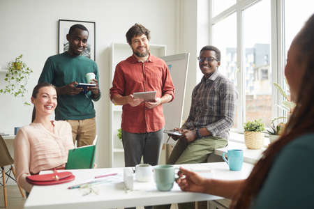 Portrait of cheerful multi-ethnic team talking to boss or manager during business meeting in office,...