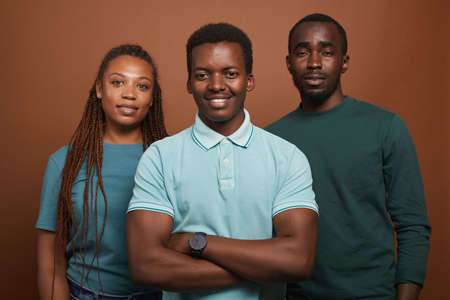 Minimal waist up portrait of three African-American people smiling at camera while standing against brown background in studioの写真素材