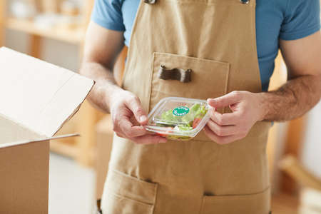 Close up of unrecognizable man wearing apron packaging individual food portions, food delivery...