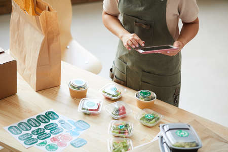 High angle close up of unrecognizable worker using digital tablet while packaging orders in food...