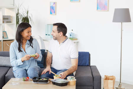 Portrait of smiling man and woman chatting cheerfully while enjoying takeout lunch in office or at home, copy spaceの写真素材