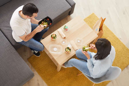 Above view portrait of man and woman eating takeout lunch in office or at home while sitting on big couch, copy spaceの写真素材